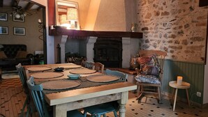 Un coin repas avec une table en bois et des chaises bleues, une cheminée et un mur en pierre.