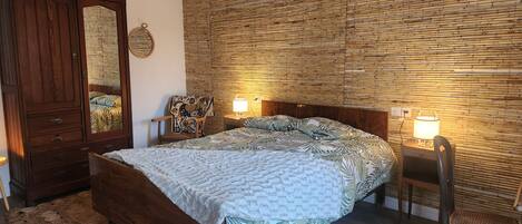 Een slaapkamer met een houten bed, een nachtkastje met lamp, een stoel en een kledingkast.