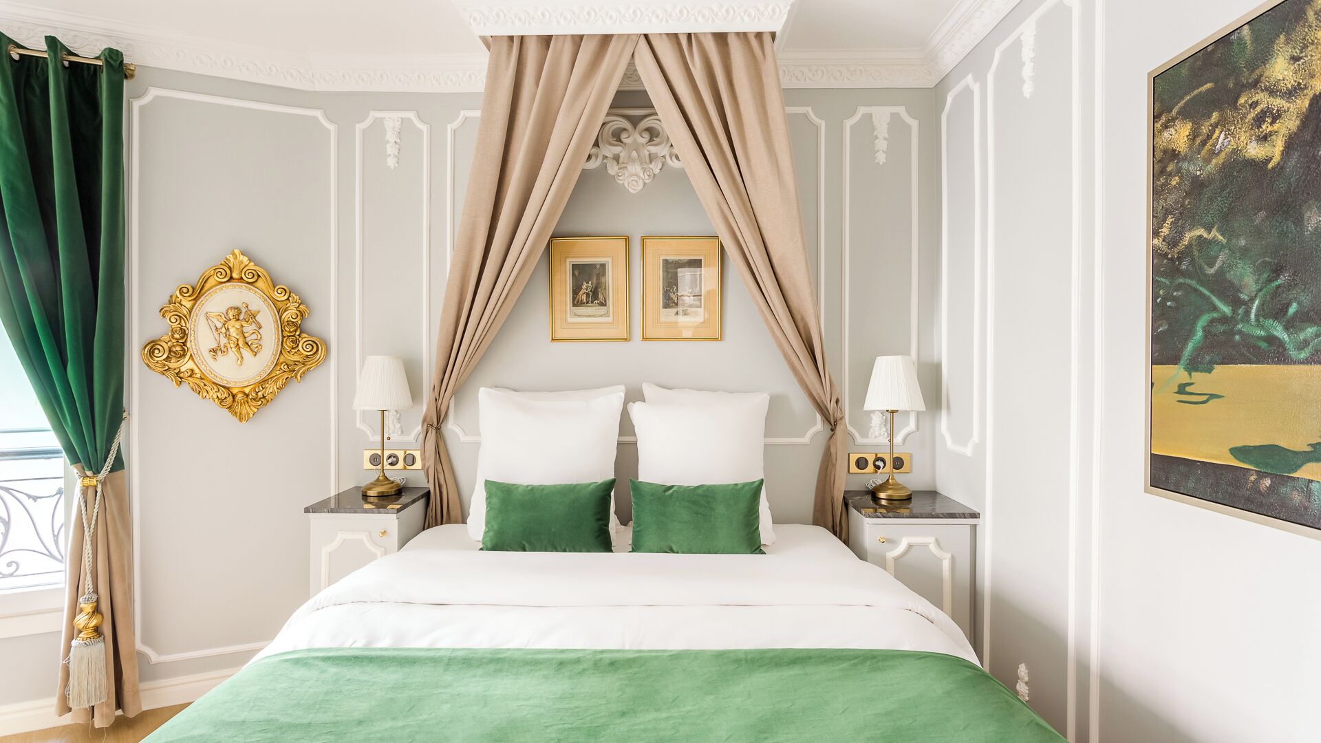 A bedroom with a canopy bed, two bedside tables with lamps, a gold-framed mirror, and two framed pictures on the wall.