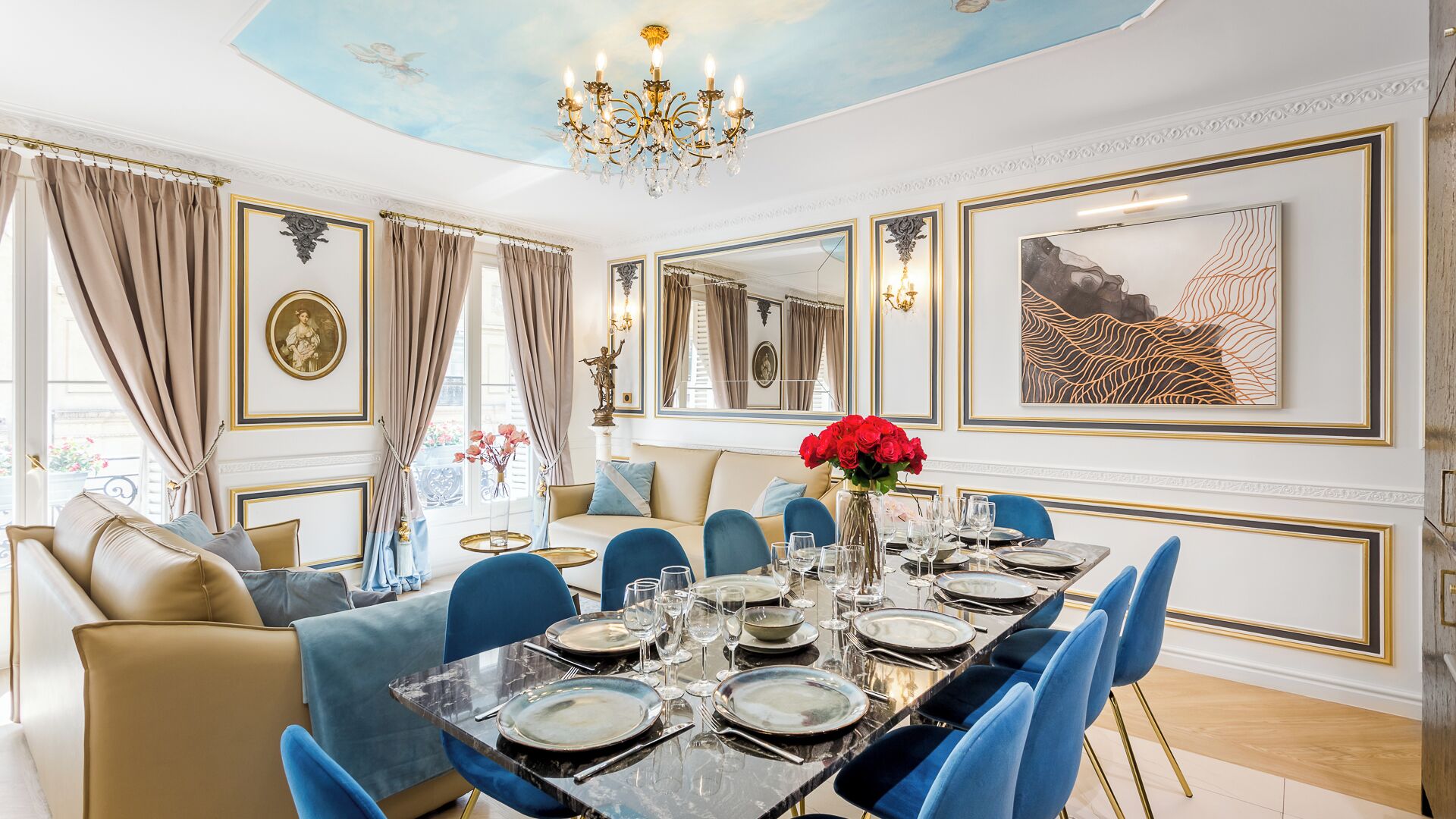 A dining room with a marble table set for six, blue upholstered chairs, and a chandelier.