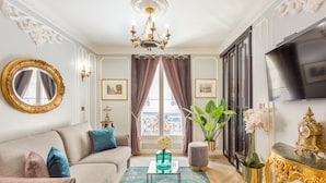 Una sala de estar lujosa con sofá, candelabro, televisor y un amplio ventanal con cortinas.