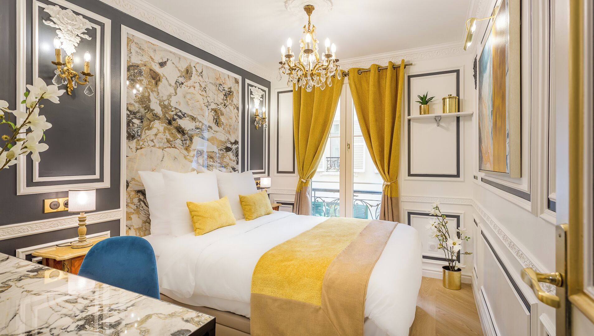 A luxurious bedroom with a large bed, a chandelier, a marble wall, and a view of the city.
