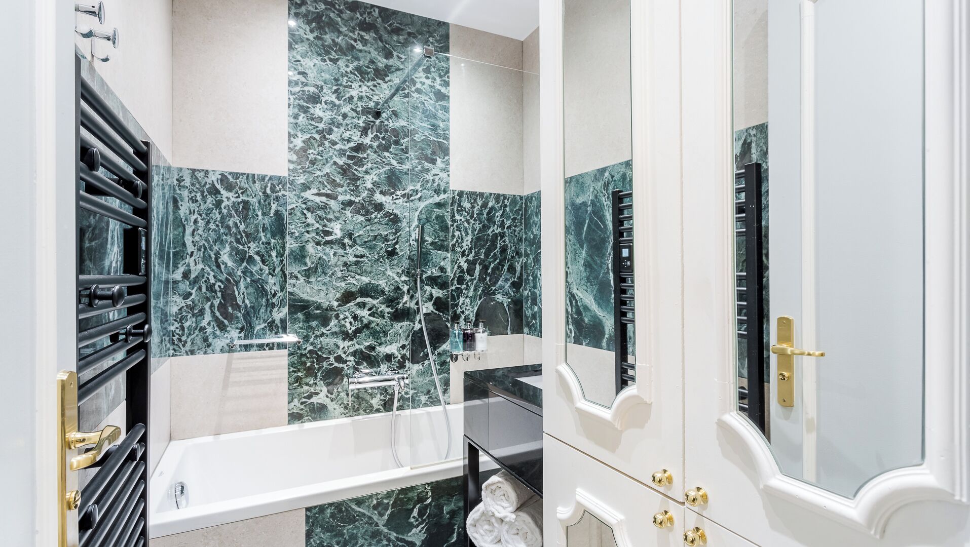 Een badkamer met een marmeren spatwand, een bad, een toilet en een wastafel.