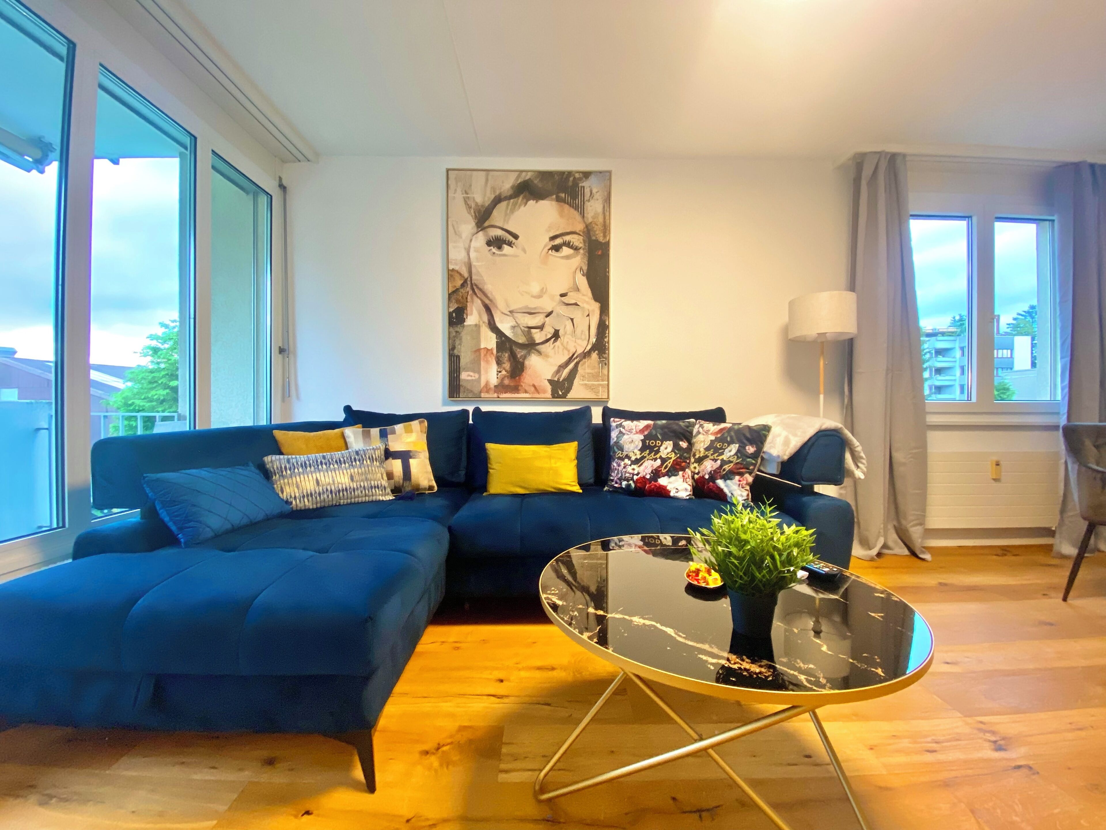 Un soggiorno moderno con un divano blu, un tavolino in vetro e un grande quadro astratto appeso alla parete.