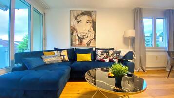 Un soggiorno moderno con un divano blu, un tavolino in vetro e un grande quadro astratto appeso alla parete.