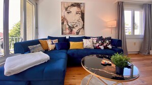 Un salon moderne avec un canapé d’angle bleu, une table basse en verre et un grand tableau abstrait accroché au mur.