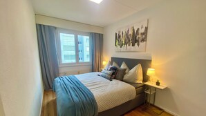 Une chambre à coucher avec un lit, une fenêtre avec des rideaux, une œuvre d’art accrochée au mur et des lampes de chevet.