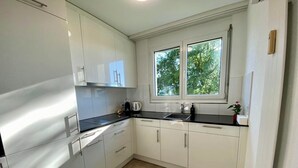 Une cuisine moderne avec des meubles blancs, un plan de travail noir et une fenêtre donnant sur la forêt.