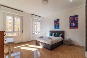 Een slaapkamer met een groot bed, twee ramen en kunstwerken aan de muur.