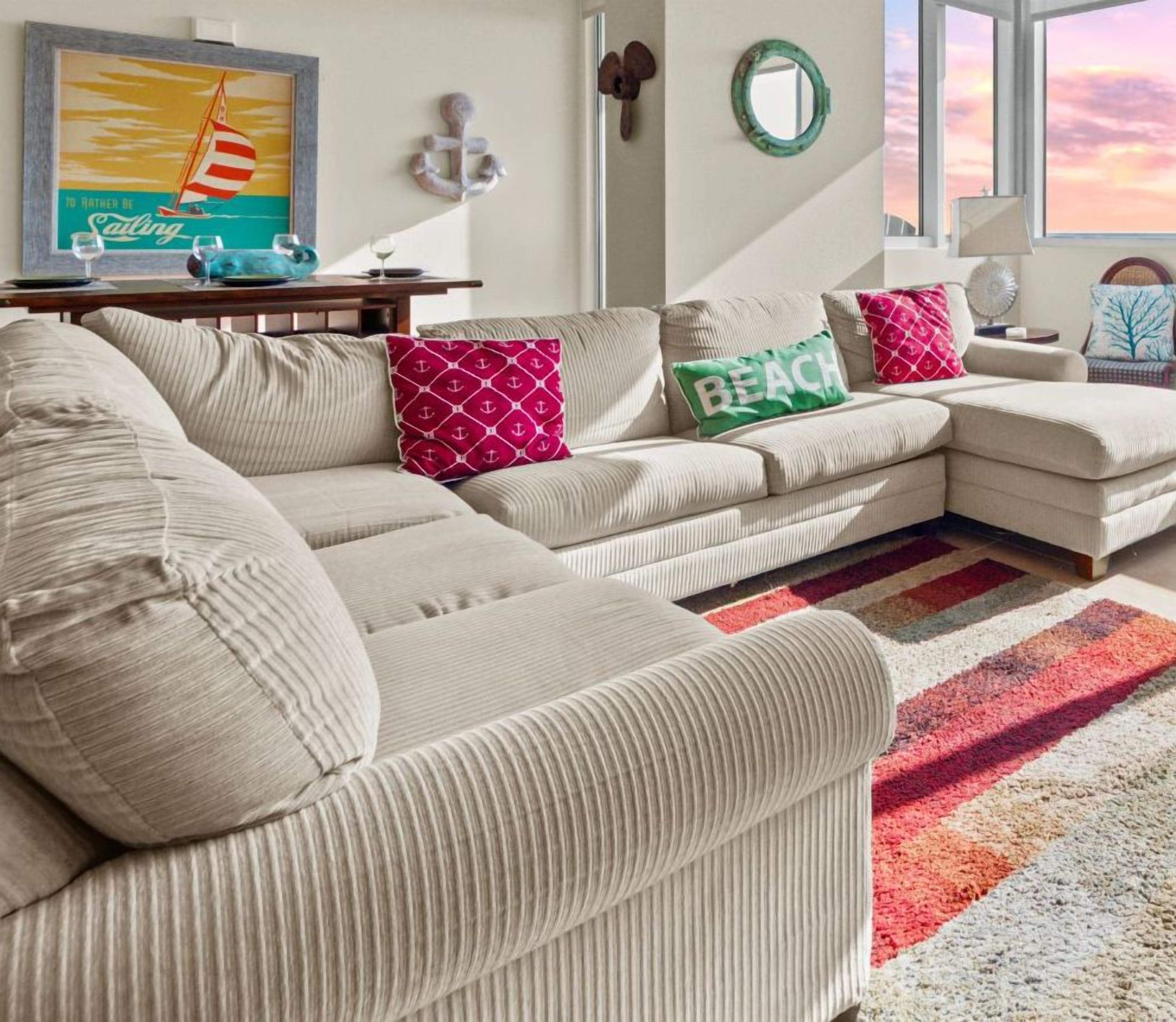 Un salon moderne avec un grand canapé d’angle, un tapis rayé aux couleurs vives et des coussins décoratifs.