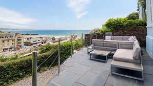 Un patio con mobiliario exterior que da a una playa y un pueblo.