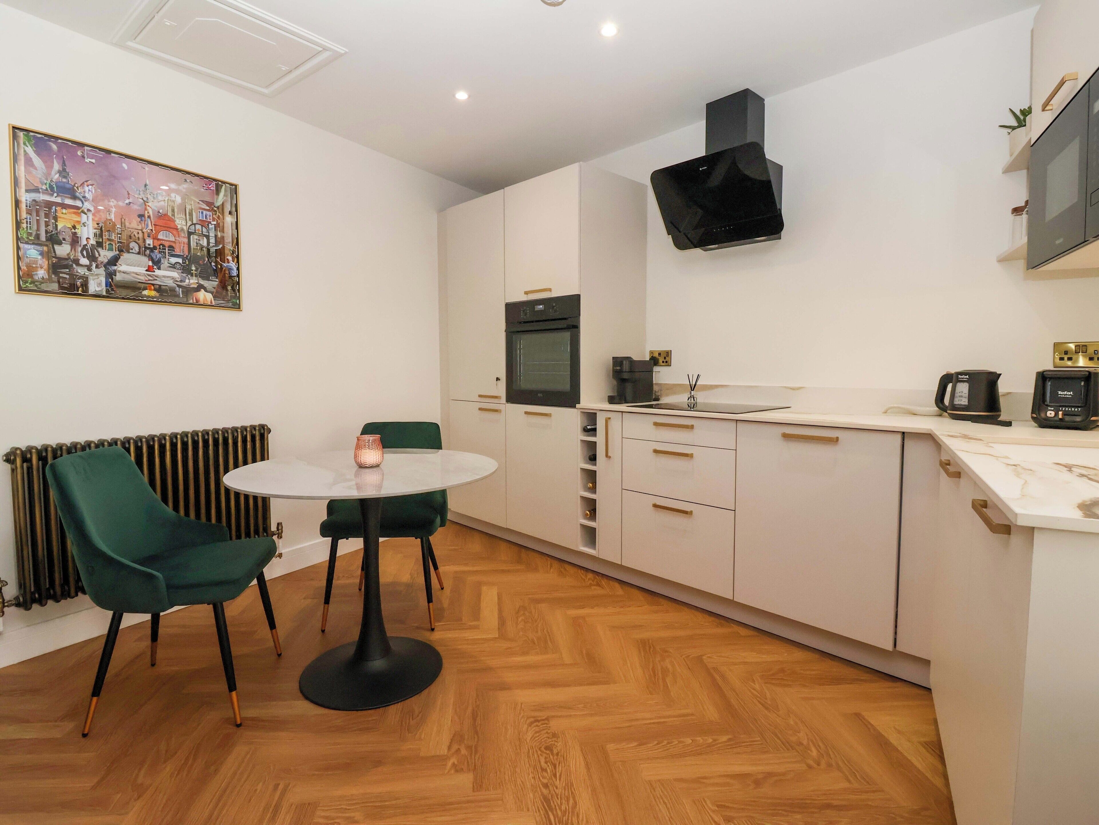 A modern kitchen with white cabinets, a black range hood, and a small dining area with a round table and green chairs.