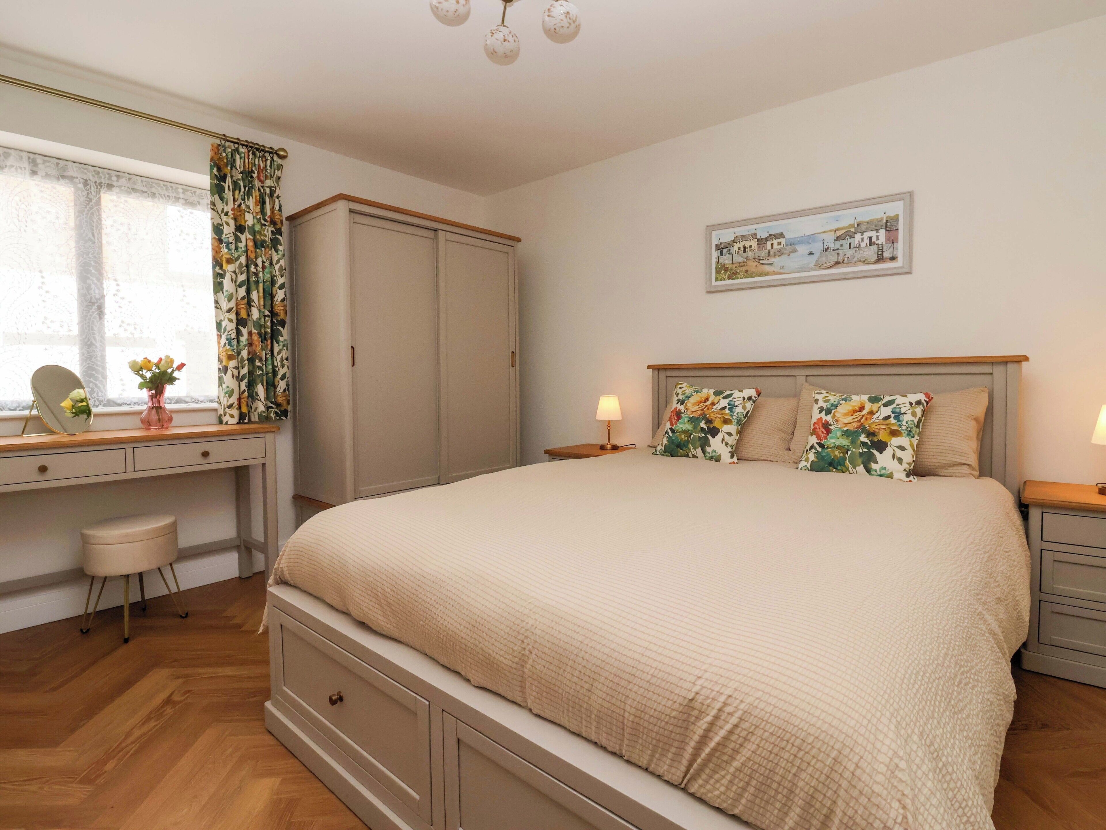 A bedroom with a bed, a desk with a mirror, a wardrobe, and a painting on the wall.