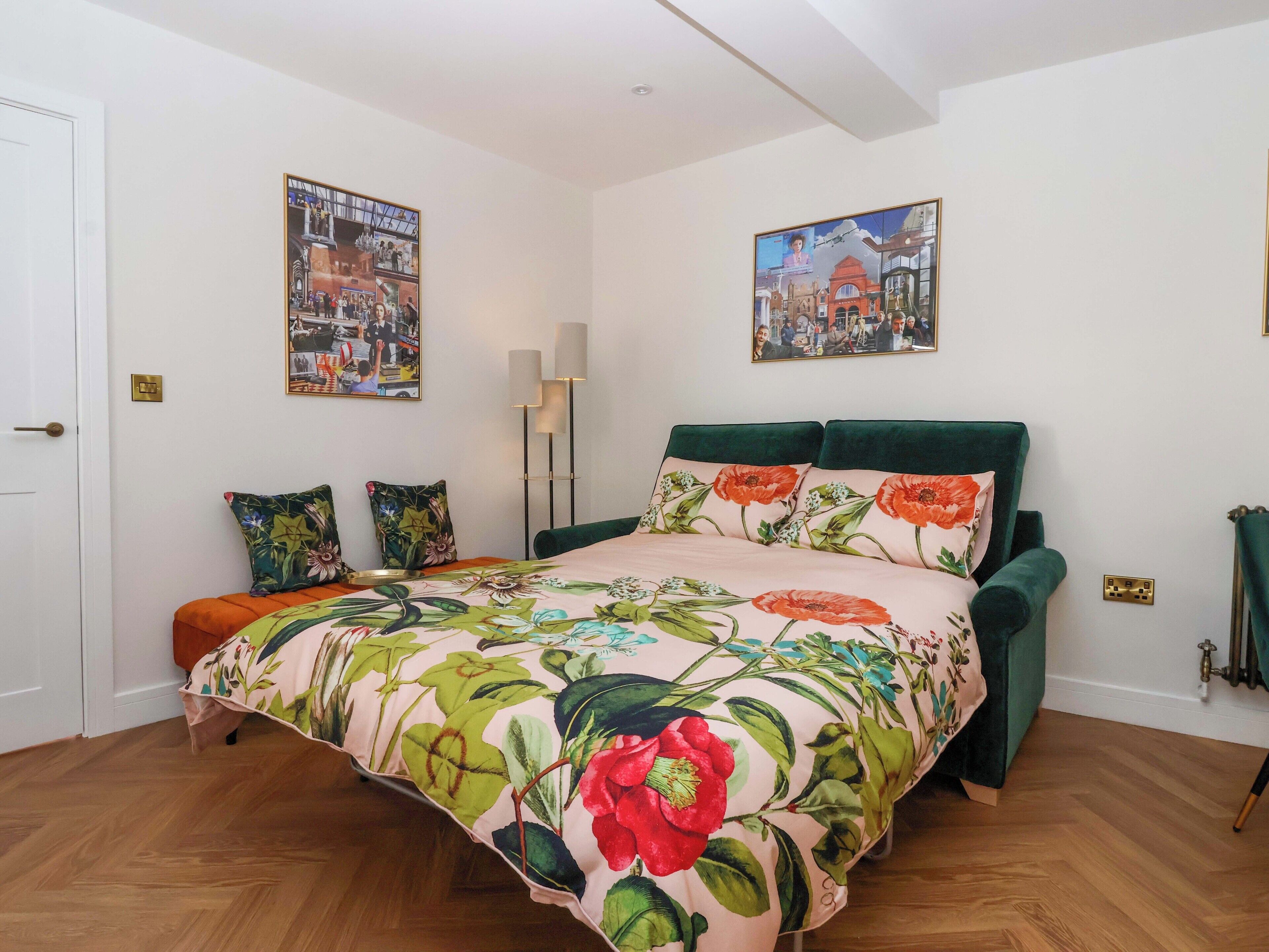 A bedroom with a floral bedspread, a green upholstered headboard, and two wall-mounted paintings.