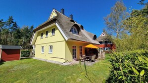Une maison jaune avec un toit de chaume et un petit patio agrémenté de mobilier d’extérieur.