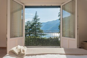 A bedroom with a large window offering a view of a mountain and a lake. - The Secret Lake View by Rent all Como (Pognana Lario)