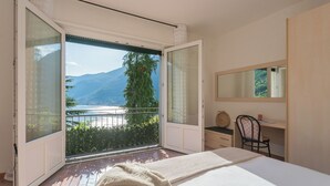 A bedroom with a balcony, a bed, a desk, and a chair.