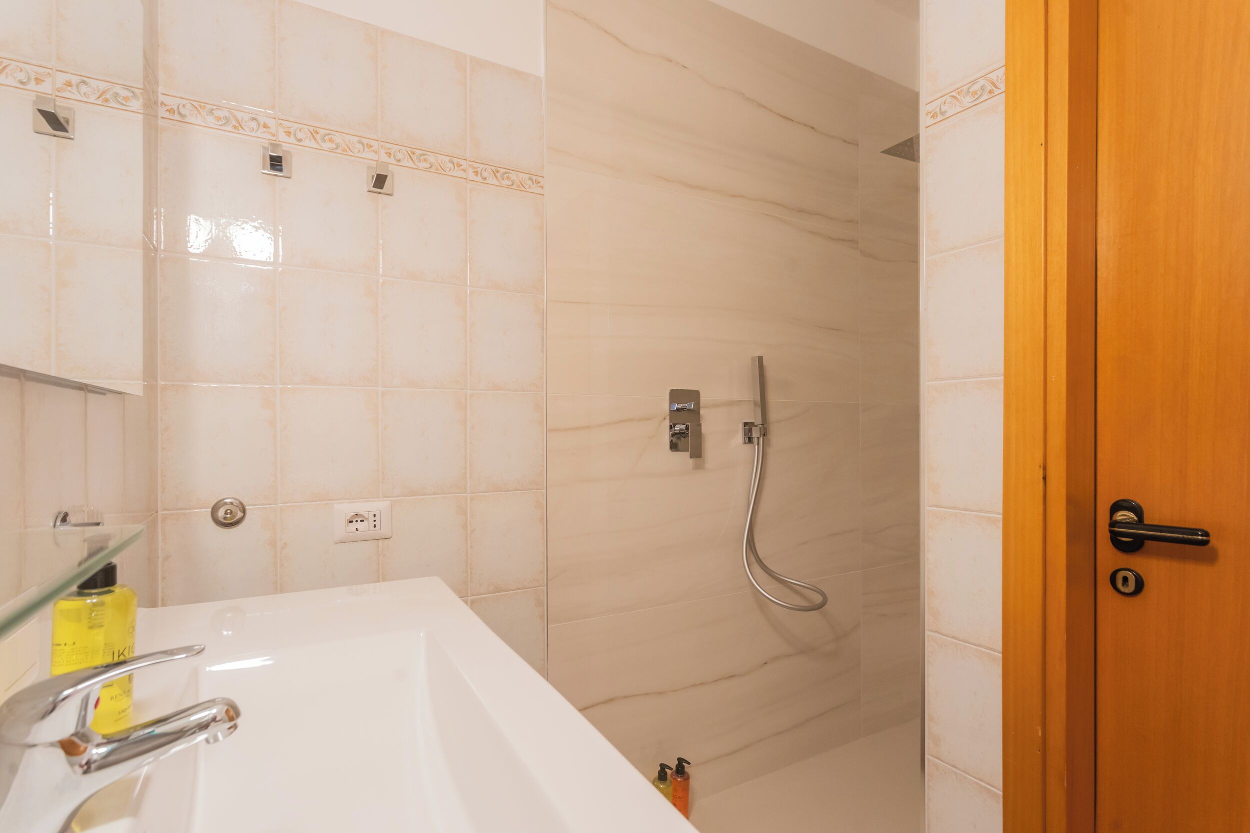 Een badkamer met een wit bad, een douche met een handdouche en een houten deur.