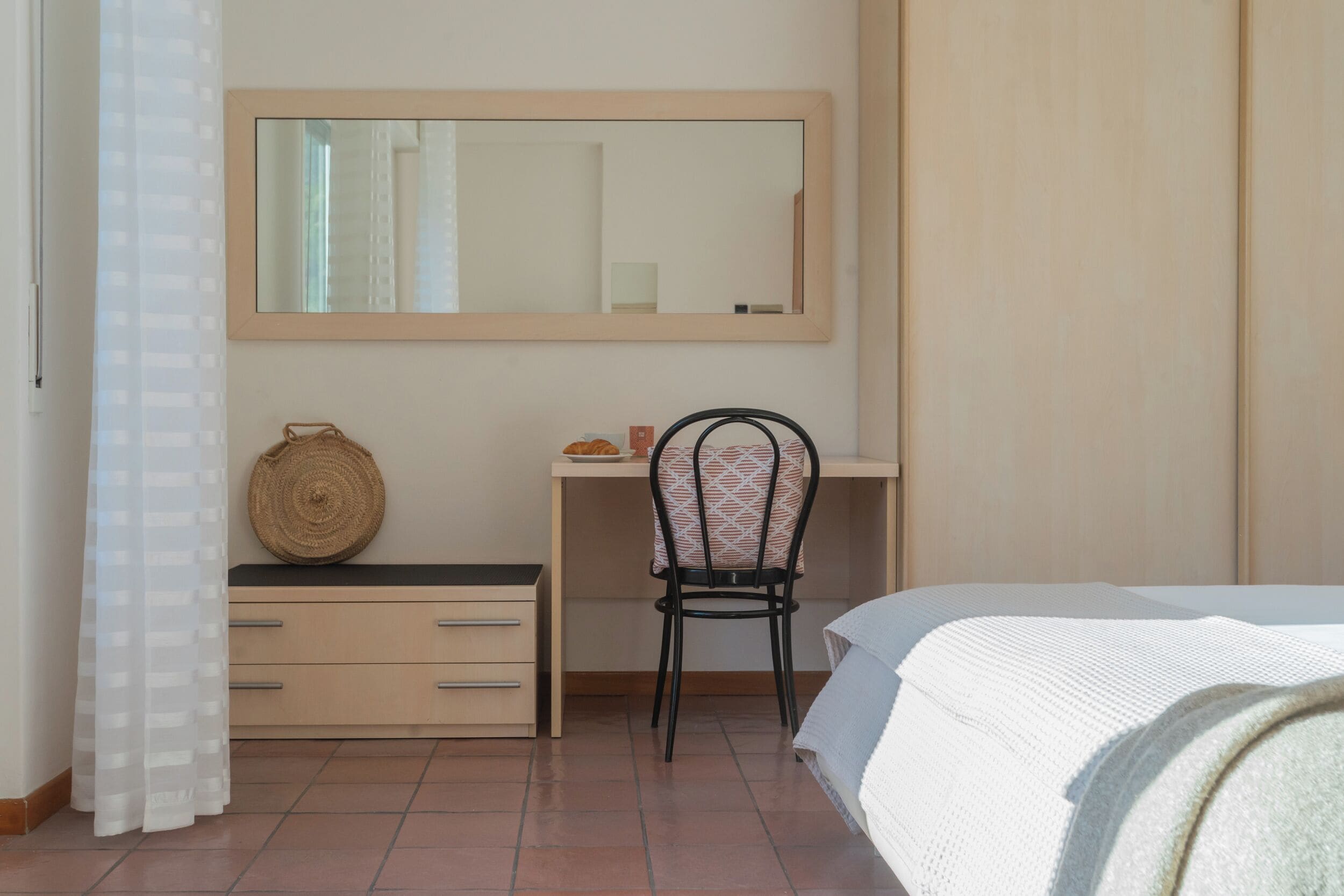 A bedroom with a bed, a desk, a chair, a mirror, and a wardrobe.