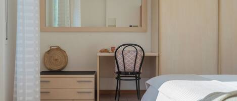 A bedroom with a bed, a desk, a chair, a mirror, and a wardrobe.