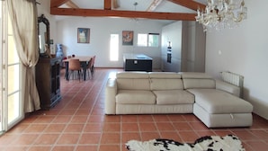 A spacious living area with a sectional sofa, a dining table with chairs, a kitchen in the background, and a chandelier. - Villa - Pool - 3 Bedrooms - Garden (Saint-Quentin-la-Poterie)