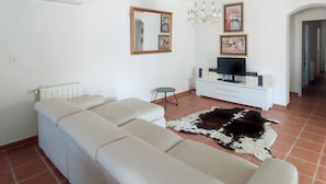 A living room with a sectional sofa, a television on a white cabinet, and a chandelier. - Villa - Pool - 3 Bedrooms - Garden (Saint-Quentin-la-Poterie)