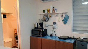A compact room with a bed, a kitchenette with a microwave, a coffee maker, and a small shelf with kitchen items. - Room w/ba AC Wi-Fi in Esperanza Apt. 1 (Vieques)