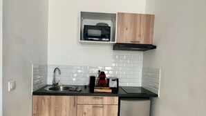 Una cocina compacta con armarios de madera, microondas integrado, refrigerador de acero inoxidable y encimera negra.