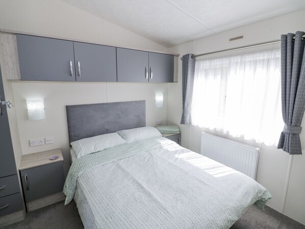 Une chambre à coucher avec un lit, des armoires grises, une table de chevet et une fenêtre avec des rideaux.