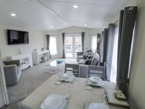 Un salon moderne avec un canapé, un téléviseur fixé au mur et un coin repas avec une table dressée pour quatre personnes.