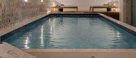 Une piscine avec un mur carrelé et deux chaises longues.