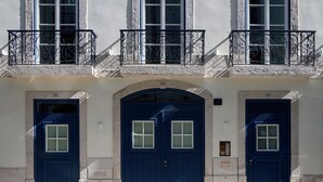 A building with three blue doors, numbered 81, 83, and 83a, and a balcony with wrought iron railings.