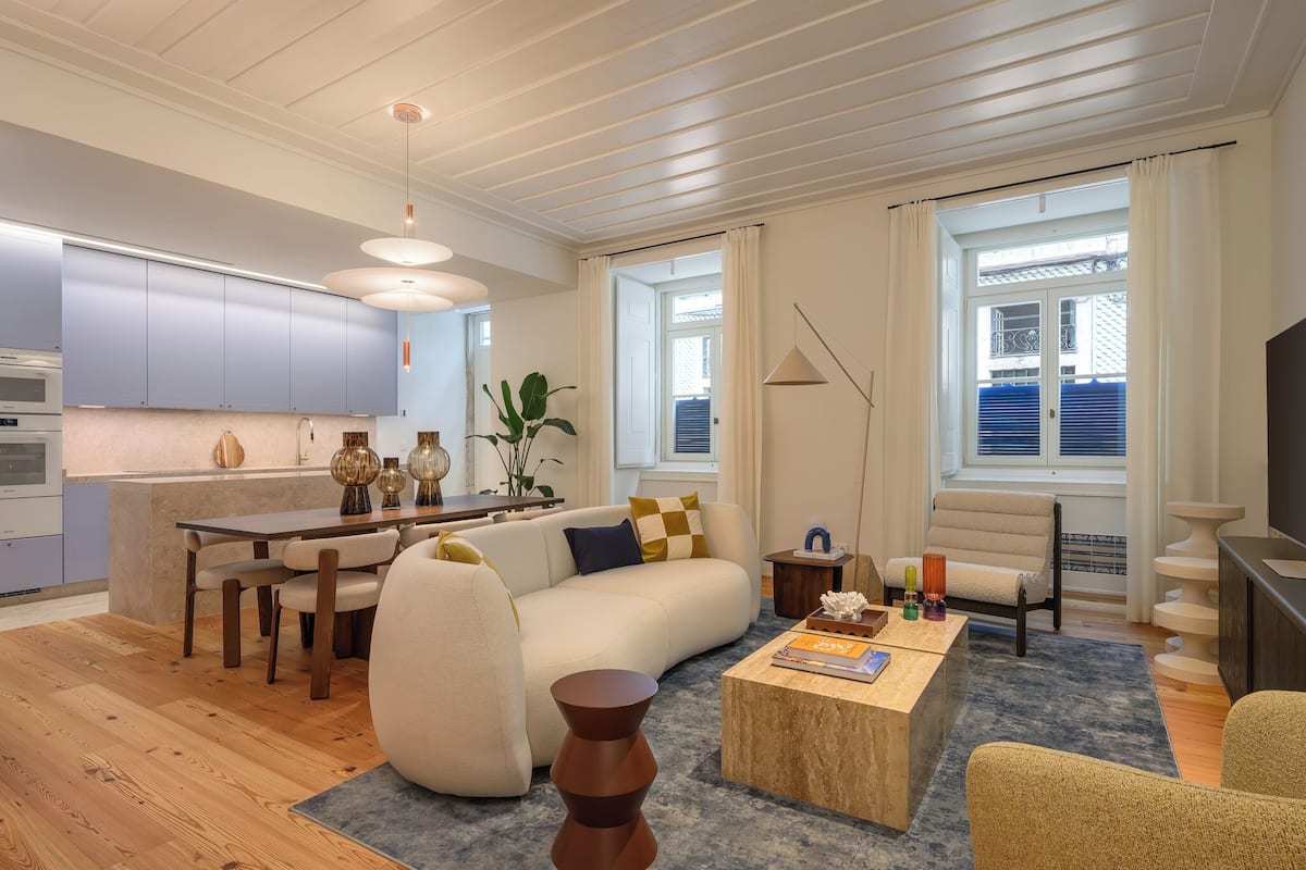 Een moderne woonkamer met een bank, salontafel en een eethoek. Er is een keuken met kasten en een raam.