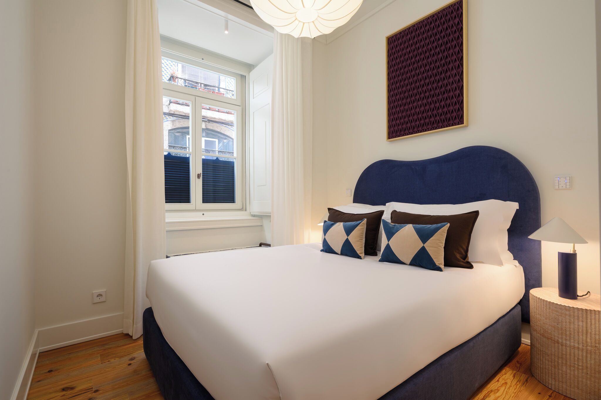 Uma cama bem arrumada com cabeceira azul, um painel de parede estampado e uma luminária de cabeceira.