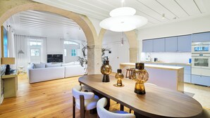 A modern kitchen with a central island, a dining area with a wooden table and chairs, and a living area with a sofa and a TV.