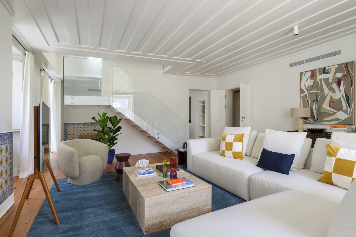 Een moderne woonkamer met een witte bank, een salontafel, een potplant en een trap naar een andere kamer.