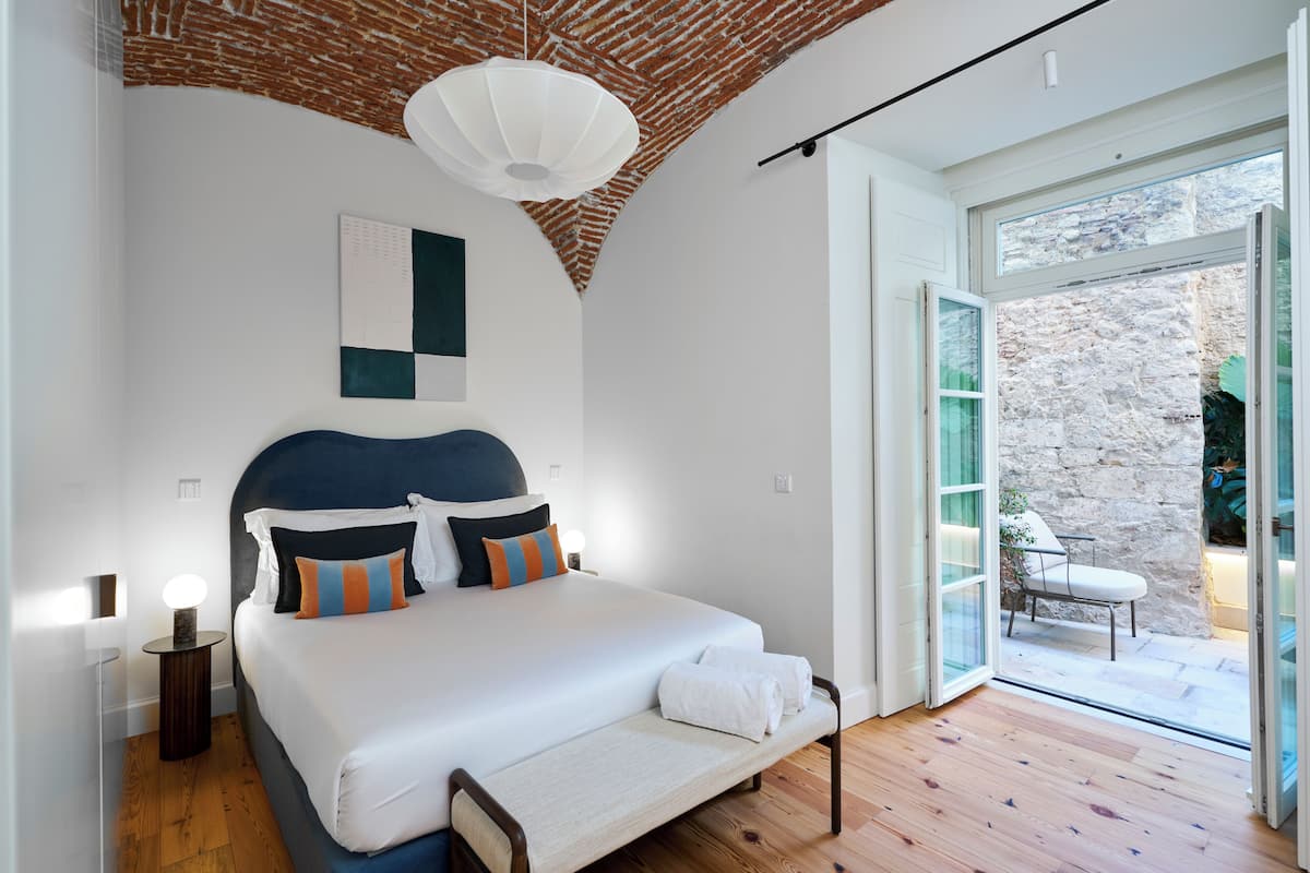 Een slaapkamer met een groot bed, een houten vloer, een bakstenen plafond en een glazen deur naar buiten.