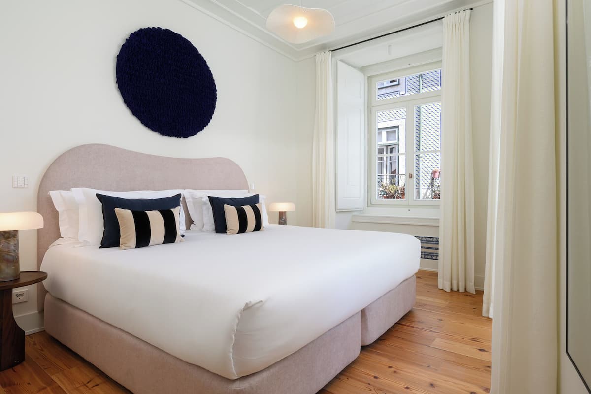 Een keurig opgemaakt bed met hoofdbord, twee bedlampjes en een ronde decoratie aan de muur.
