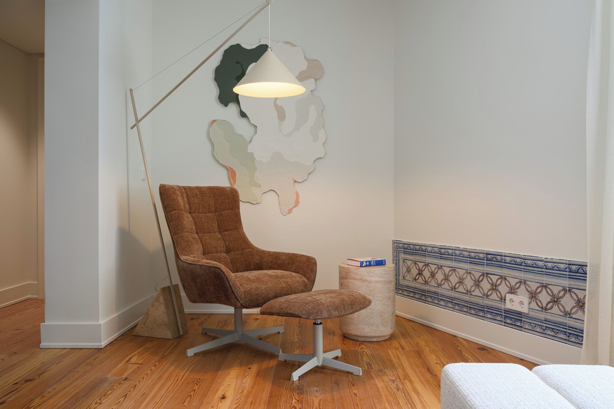 Ein modernes Zimmer mit braunem Ledersessel, einem kleinen Hocker, einer Stehlampe und einer Wanddekoration.
