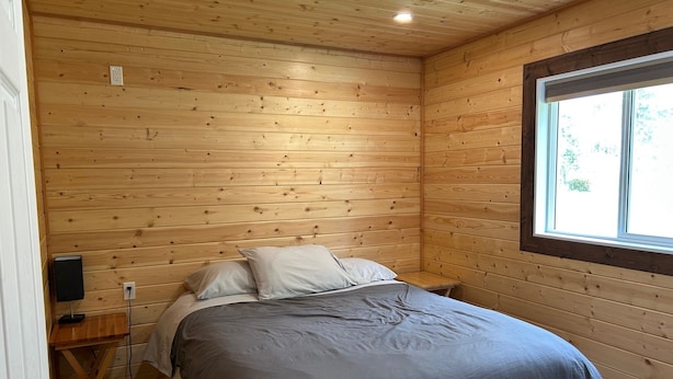 A wooden-paneled bedroom with a bed, a small table, and a window. - Cougar Mountain Lodge & Resort Ltd. (Valemount)