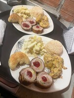 Twee borden eten met croissants, een rolletje vlees, rijst en een aardappelgerecht.