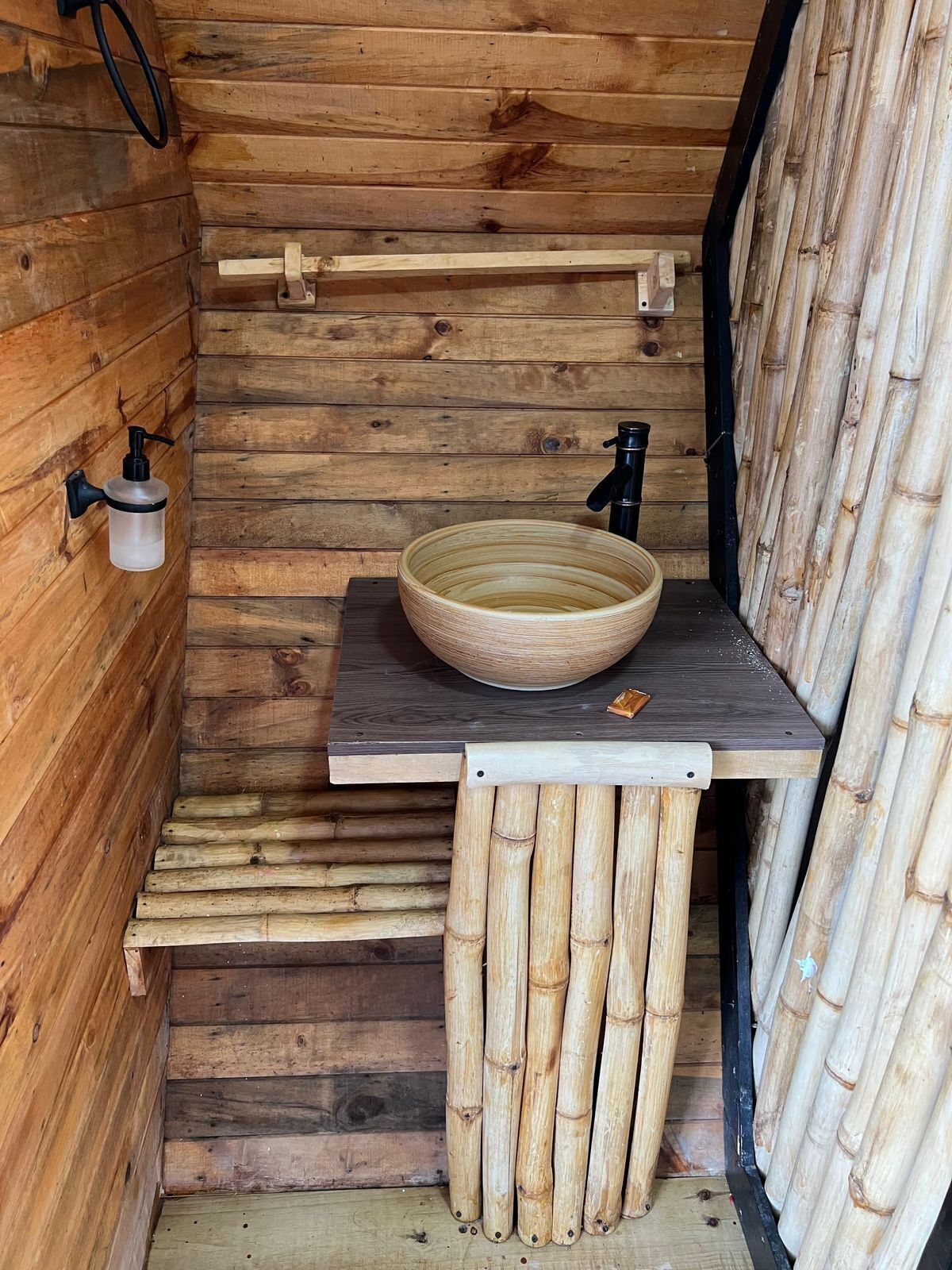 Une salle de bain rustique en bois, avec un lavabo en bois, un robinet noir et un distributeur de savon fixé au mur.