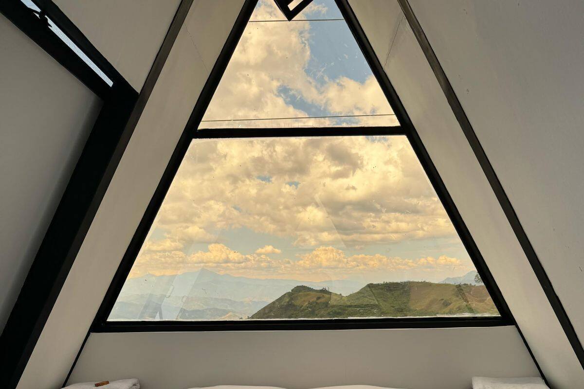 Una habitación triangular con una cama, almohadas y una botella de vino.