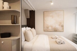 Ein Hotelzimmer mit einem Bett, Kissen, einem Nachttisch, einer Ablage mit Dekoration und einem großen, abstrakten Gemälde an der Wand.