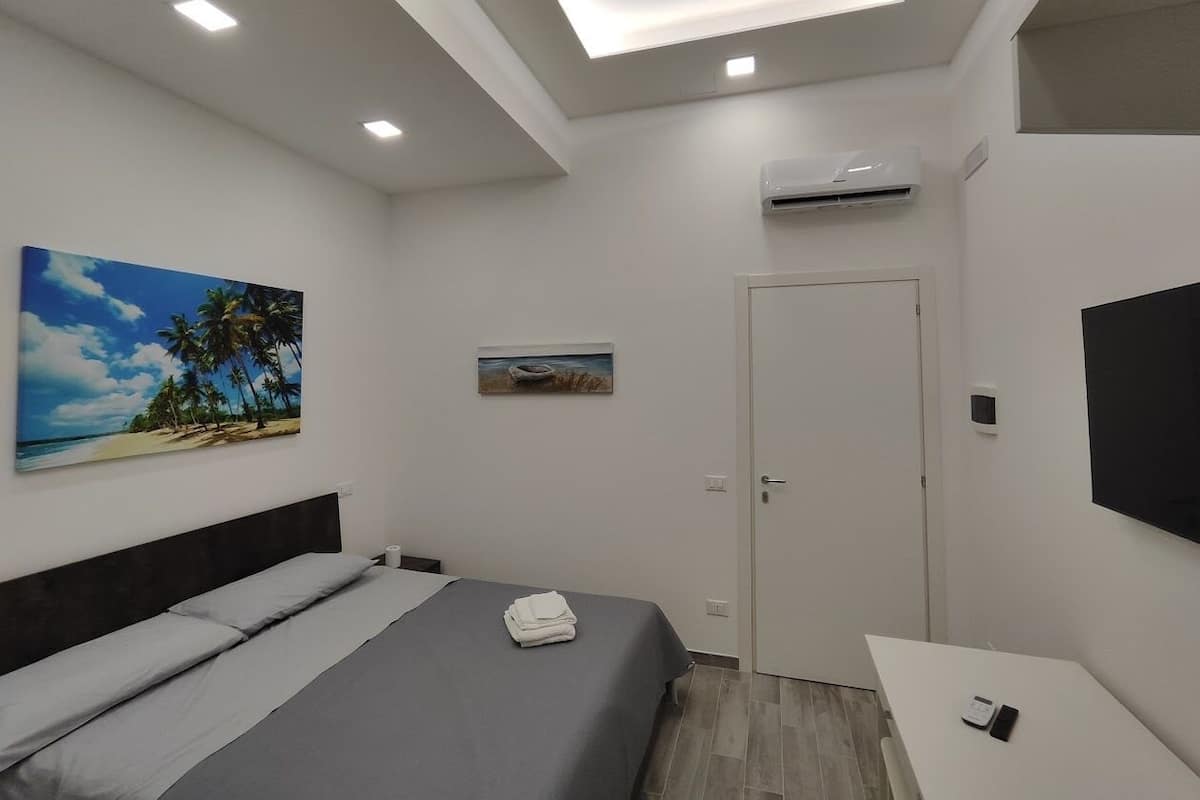 Une chambre à coucher moderne, avec un lit, une petite table de chevet, un téléviseur fixé au mur et une porte.