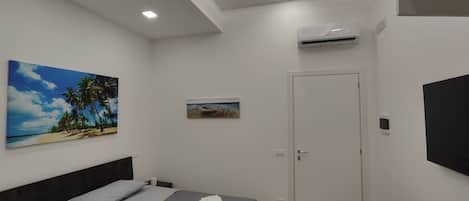 A modern bedroom with a bed, a small bedside table, a wall-mounted TV, and a door.