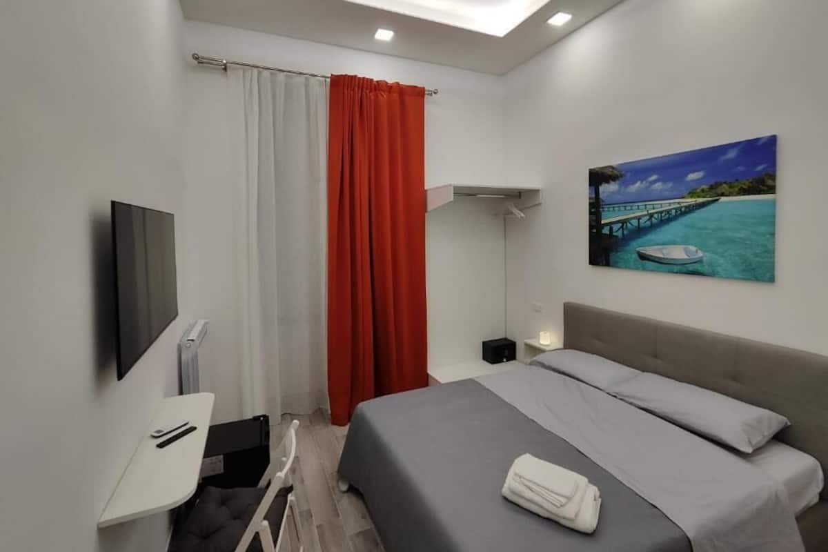 Une chambre d’hôtel moderne équipée d’un lit, d’un bureau, d’une télévision et d’un tableau représentant une jetée.