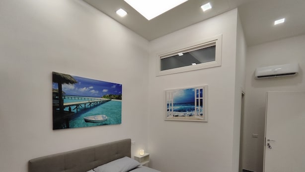 A bedroom with a bed, a painting of a beach scene, a window with a view of the sea, and an air conditioning unit. - b&b Il Regno delle due Sicilie (Naples)