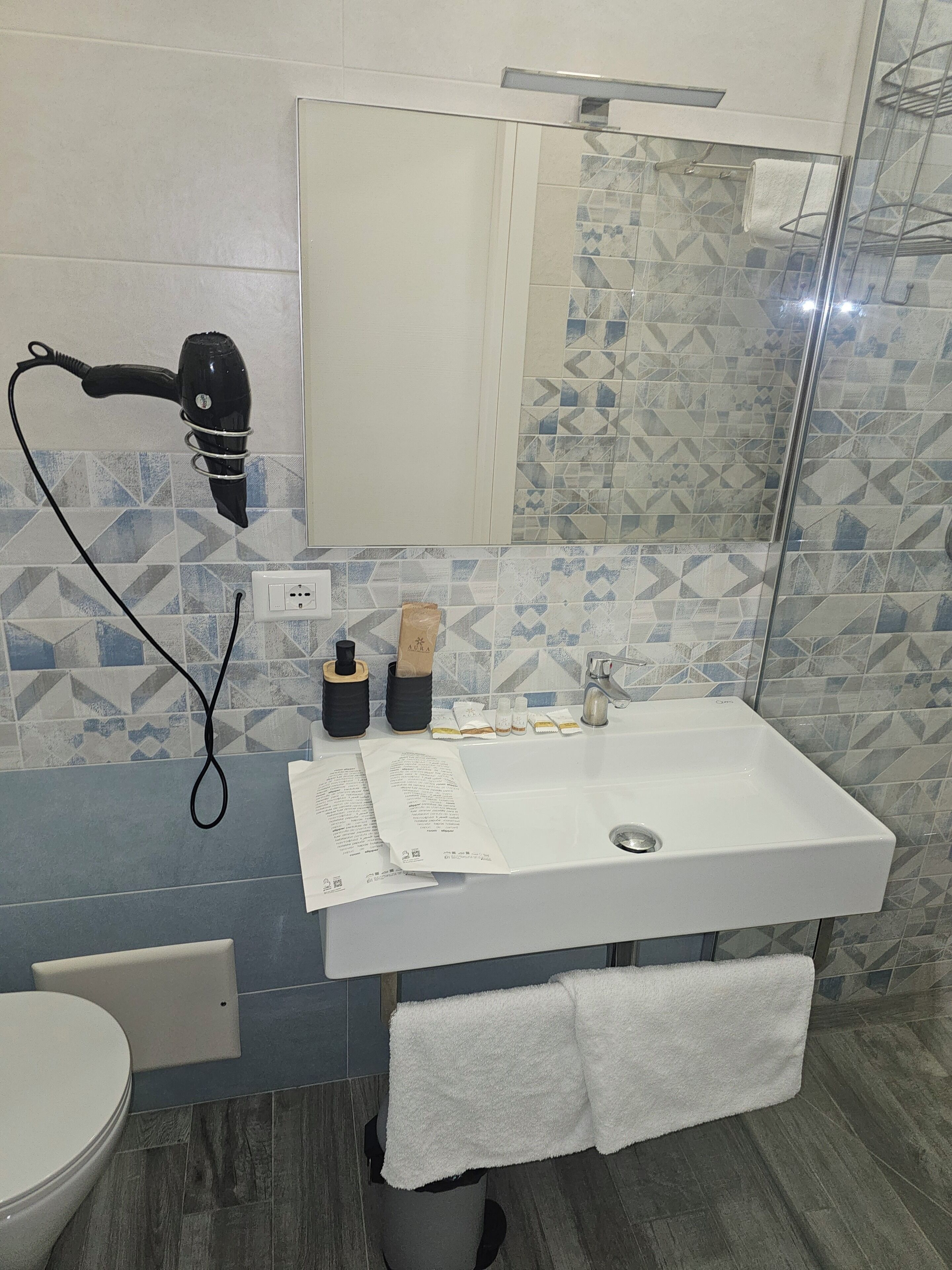 Ein Badezimmer mit einem weißen Waschbecken, einem Handtuchhalter, einem Fön und einem Spiegel.