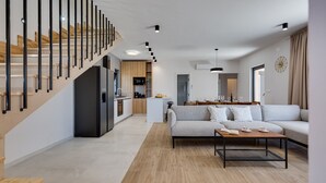A modern living space with a staircase, a kitchen, a dining area, and a sofa.